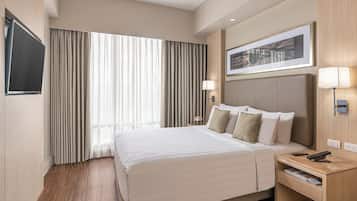 Una camera d'albergo con un letto grande, una TV a schermo piatto montata a parete, un comodino con una lampada e un quadro incorniciato sopra il letto.