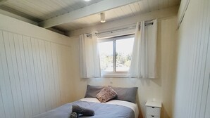 A bedroom with a single bed, a nightstand, a window with curtains, and a wooden ceiling. - Beachouse  (Loch Sport)