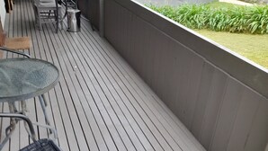 A wooden deck with a table and chairs, a grill, and a small trash can. - Beachouse  (Loch Sport)