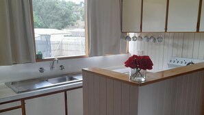 A kitchen with a window, a sink, cabinets, and a countertop with a vase of flowers. - Beachouse  (Loch Sport)