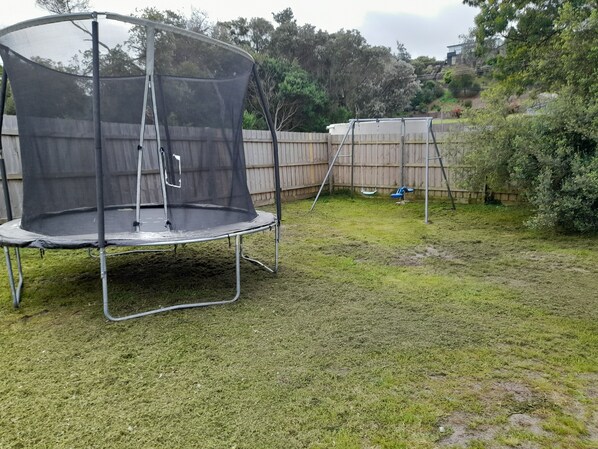 Un jardin avec un trampoline et une balançoire.