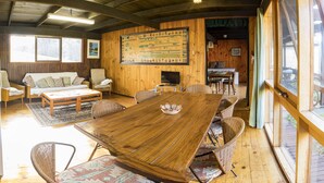 A wooden interior with a large dining table, wicker chairs, a sofa, and a television. - Beachouse  (Loch Sport)