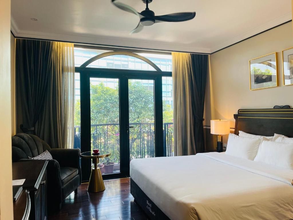 A hotel room with a bed, a chair, a small table, a ceiling fan, and a balcony with curtains.