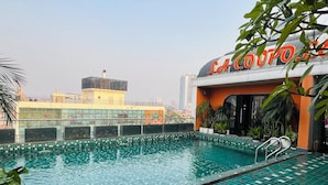 A rooftop swimming pool with a view of the cityscape, a building with a sign reading "LA COUTO", and some potted plants around the pool area.