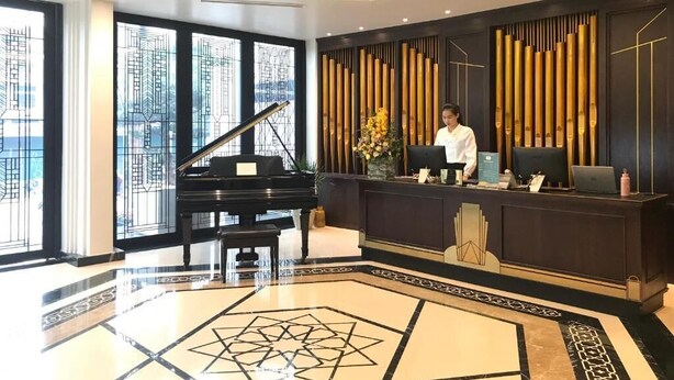 A hotel lobby with a grand piano, a reception desk, and a modern chandelier.