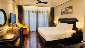 A hotel room with a large bed, a desk with a chair, a desk lamp, a television, and a ceiling fan.