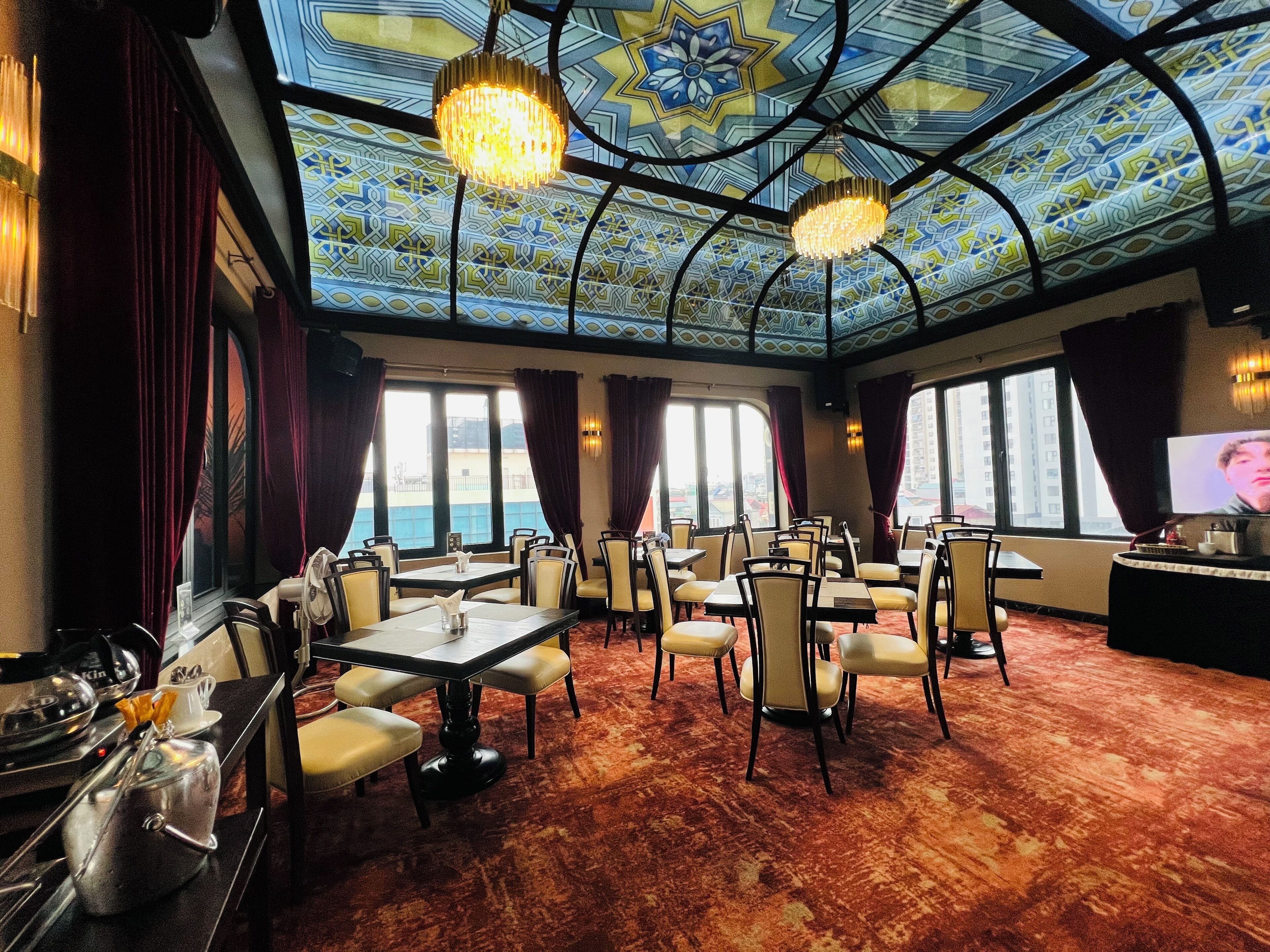 Un comedor amplio con mesas y sillas, ventanas grandes y un techo decorativo.