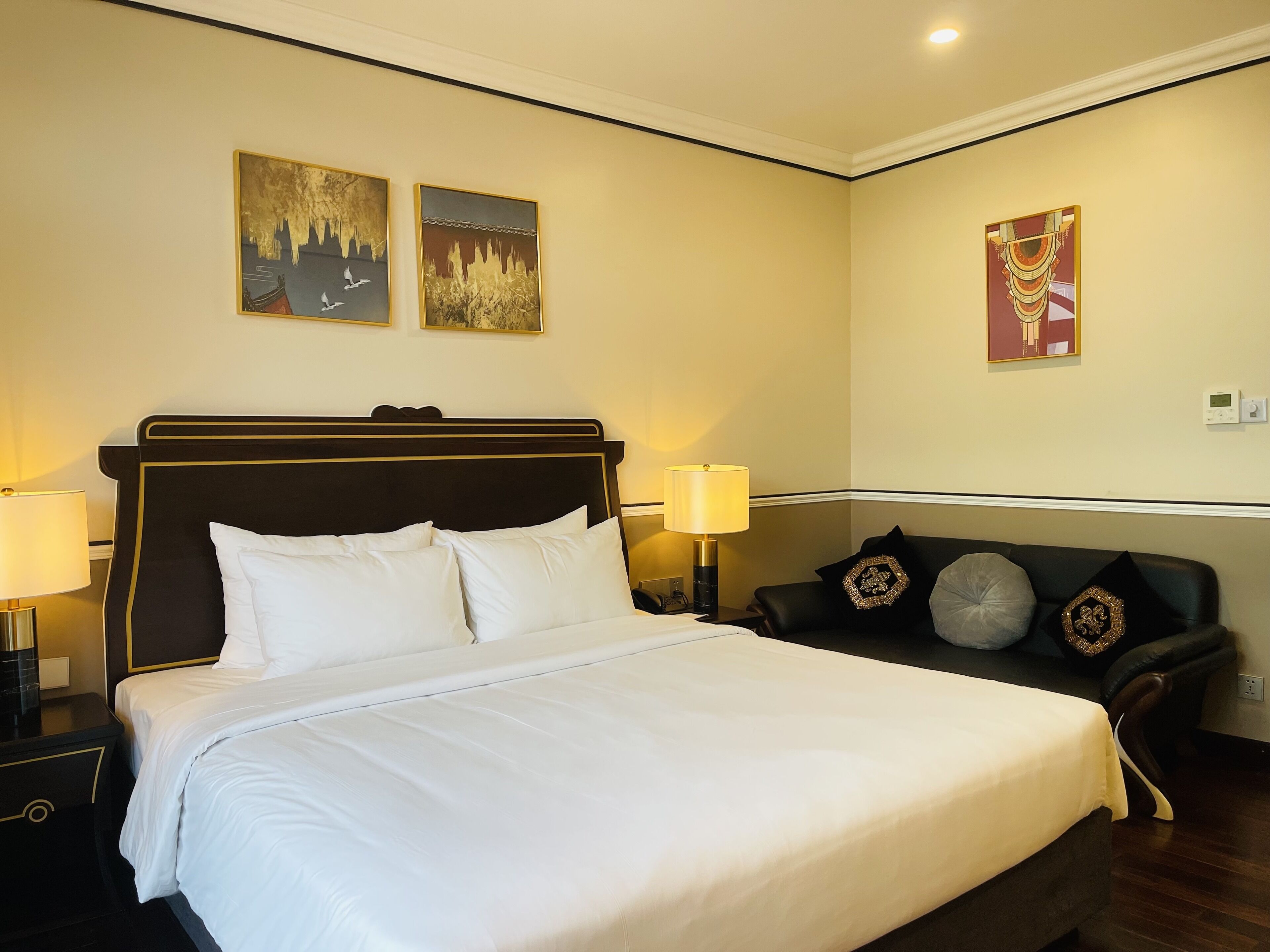 Een hotelkamer met een groot bed, twee nachtkastjes, een bank met decoratieve kussens, en drie aan de muur bevestigde schilderijen.