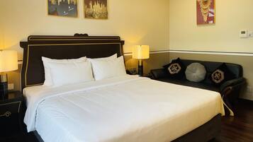 Een hotelkamer met een groot bed, twee nachtkastjes, een bank met decoratieve kussens, en drie aan de muur bevestigde schilderijen.