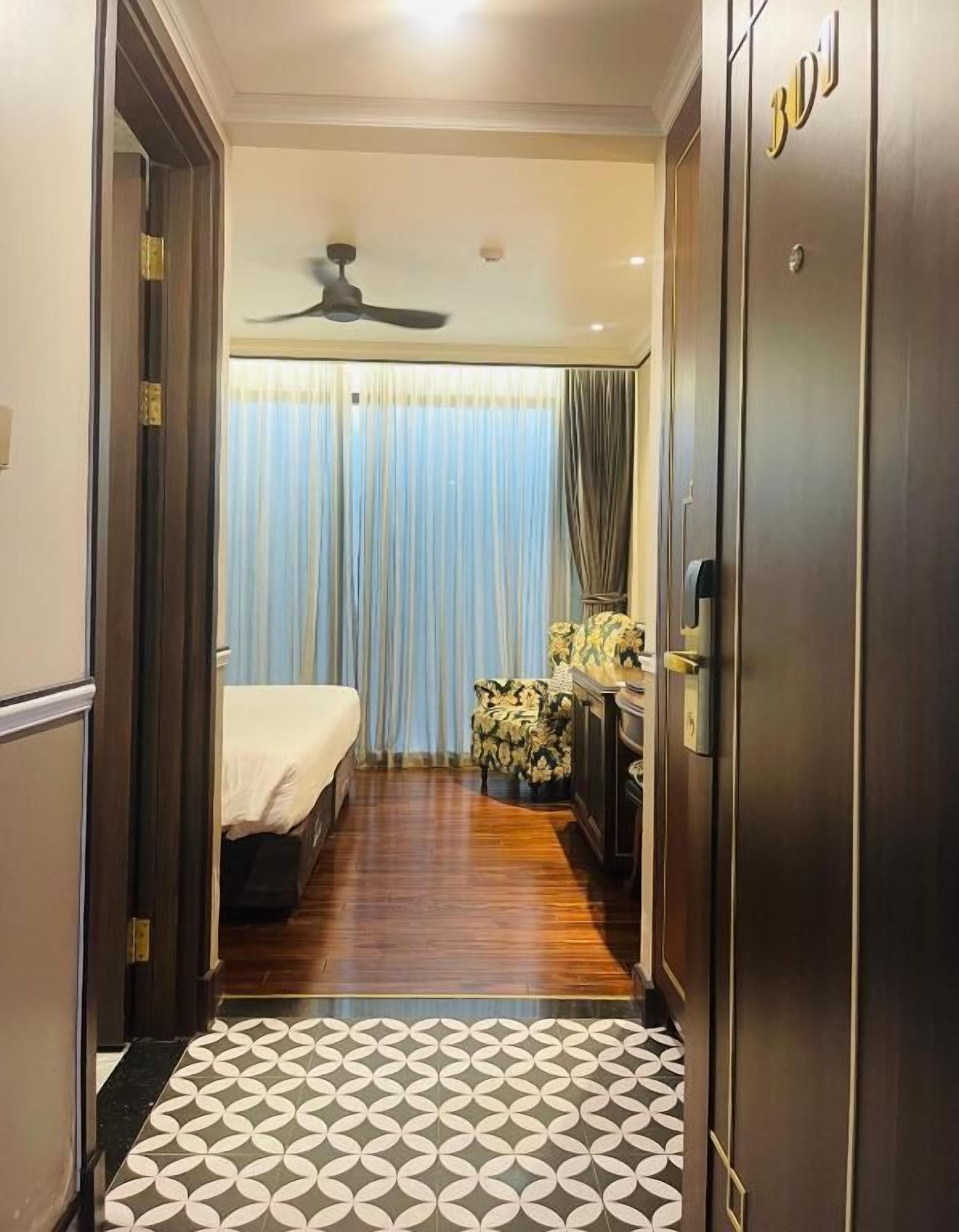 A hotel room with a bed, a desk, a chair, a ceiling fan, and a patterned floor.