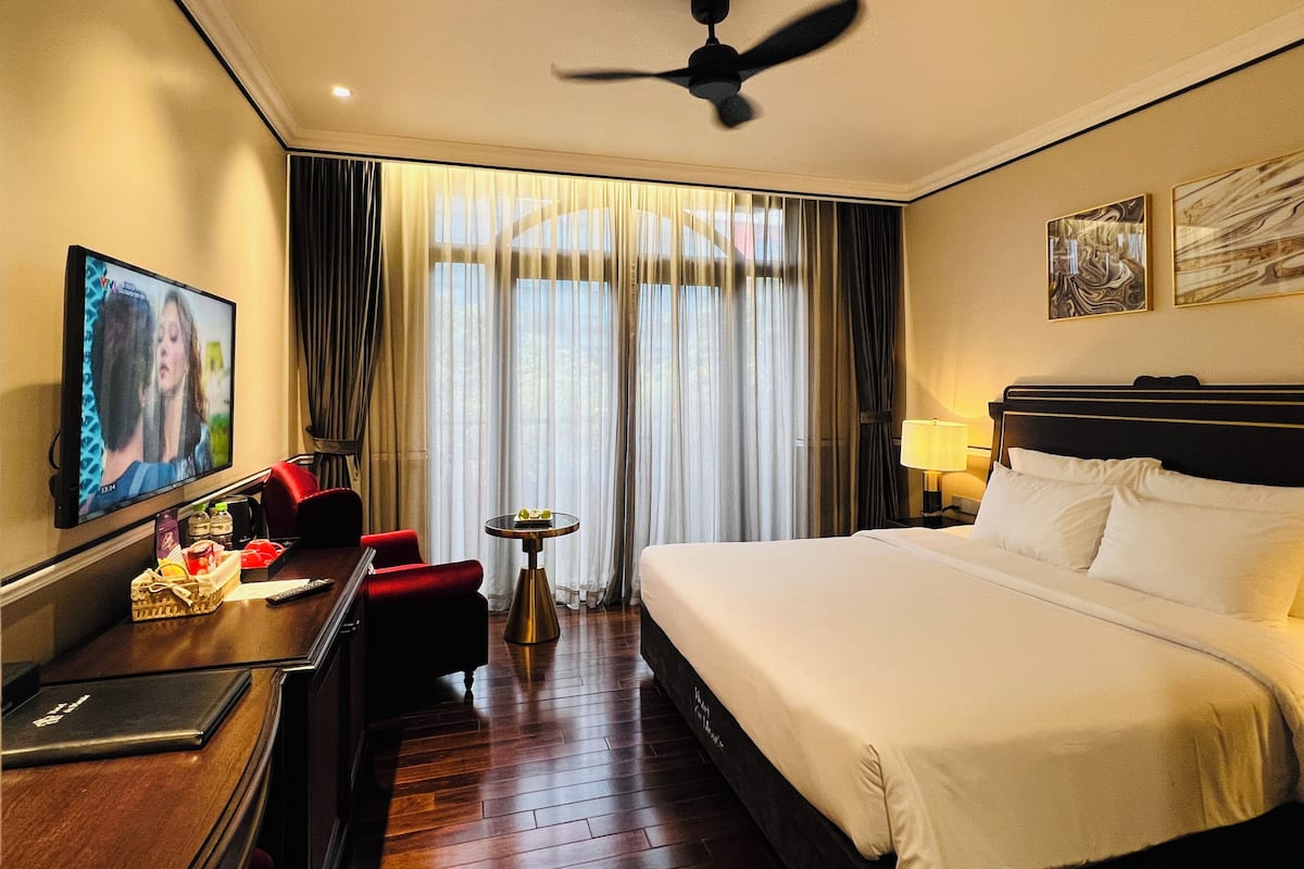 A hotel room with a bed, a desk with a computer, a television, and a ceiling fan.