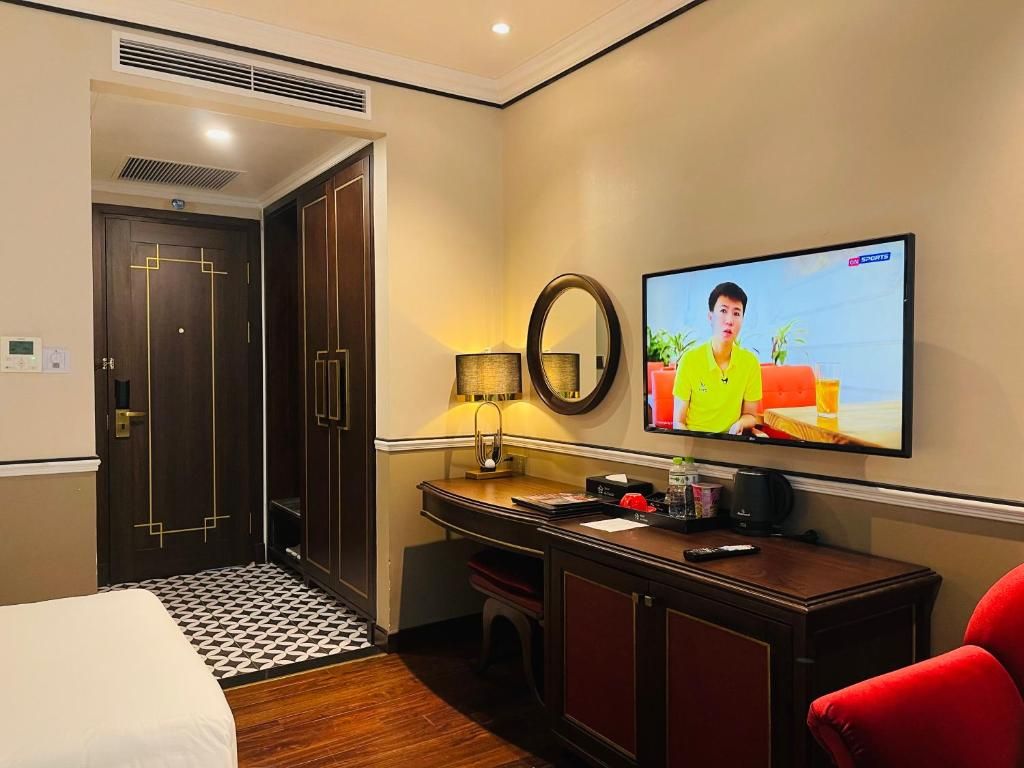 A hotel room with a bed, a desk, a television, and a red chair.