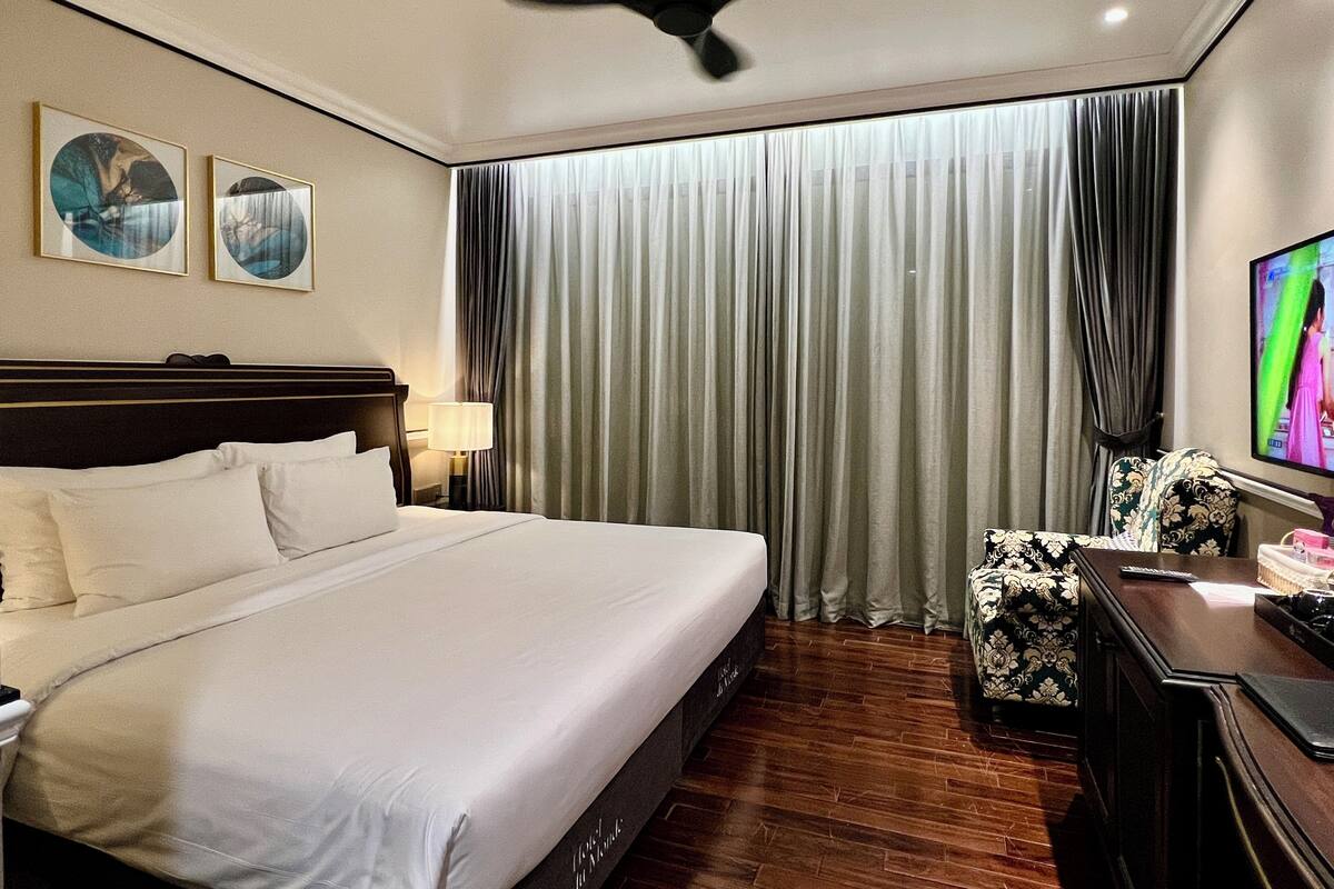 A hotel room with a bed, a desk, a chair, a television, and a ceiling fan.