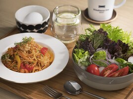 Une table à manger avec une assiette de pâtes, un saladier de salade, une tasse de café et un verre d’eau.
