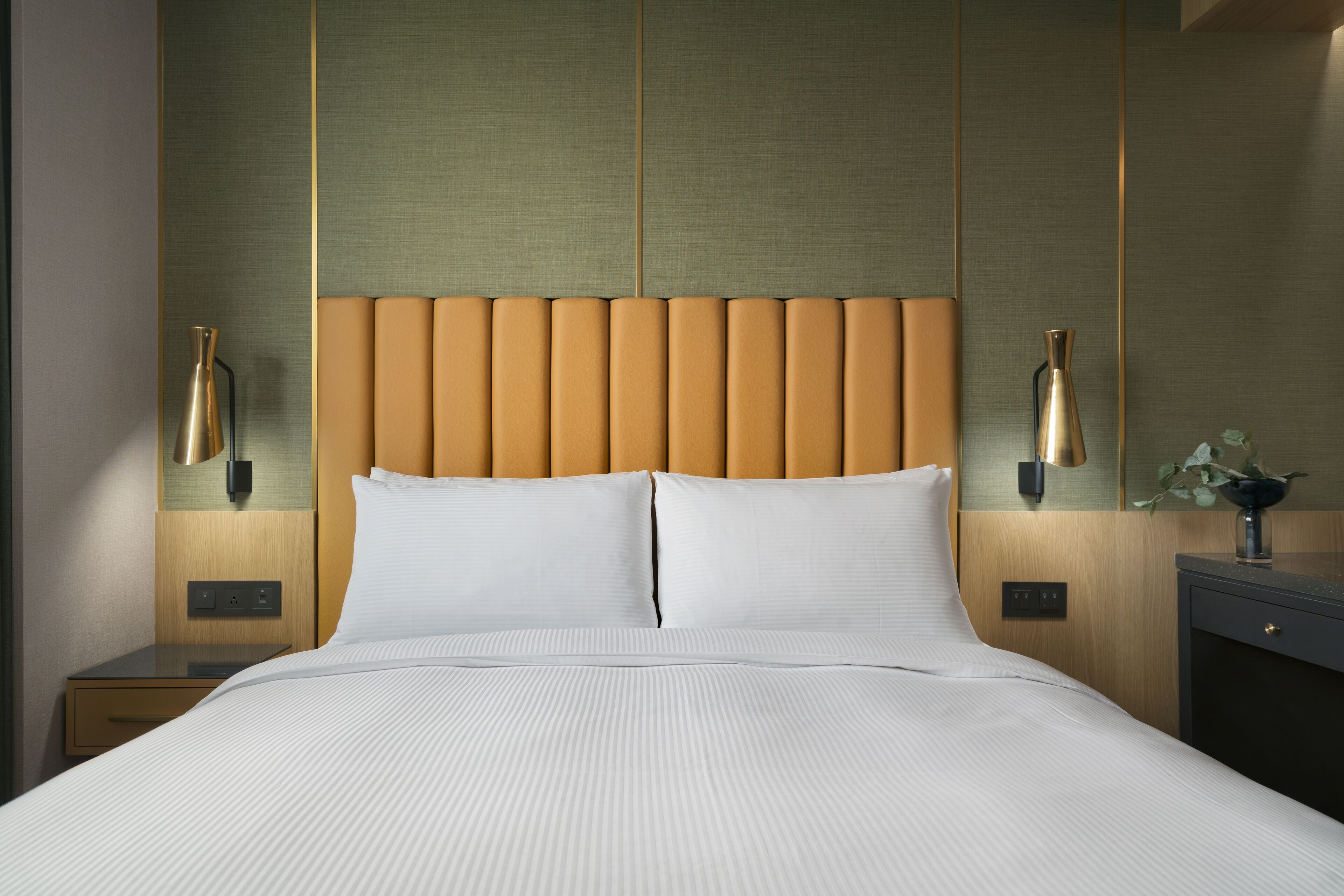 Una cama bien hecha con cabecera, mesitas de noche y lámparas fijadas a la pared.