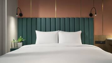 A modern bedroom with a teal headboard, white bedding, and a small plant on a bedside table.