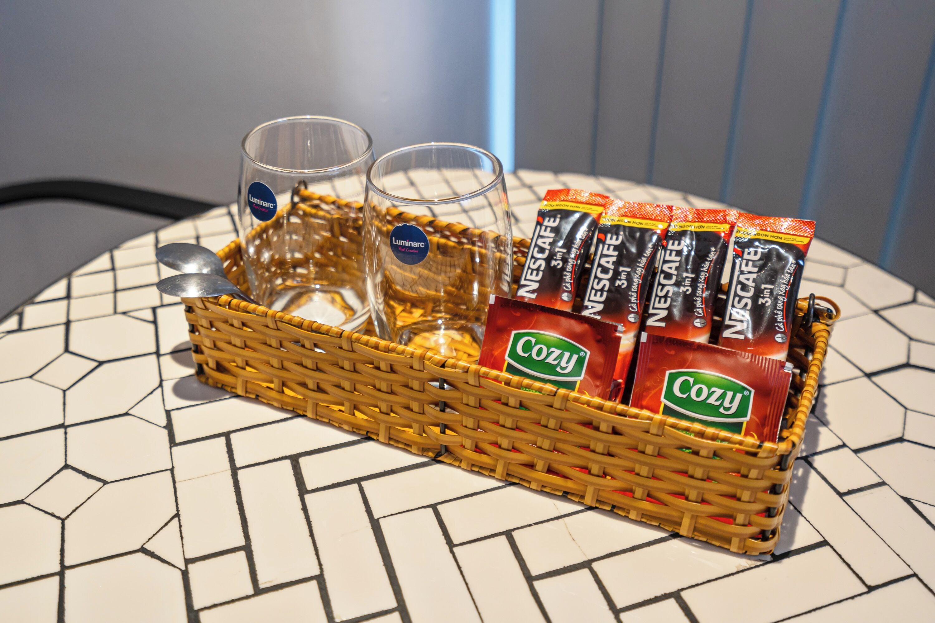 A wicker basket containing two glasses, a spoon, and several packets of Nescafe coffee.