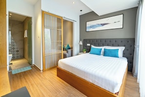 A modern bedroom with a large bed, a grey headboard, and a painting of a seascape.
