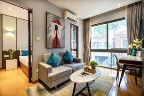 A modern living room with a sofa, a coffee table, a dining table, and a large window with a view. - The Art - Sunshine Apartment (Ho Chi Minh City)