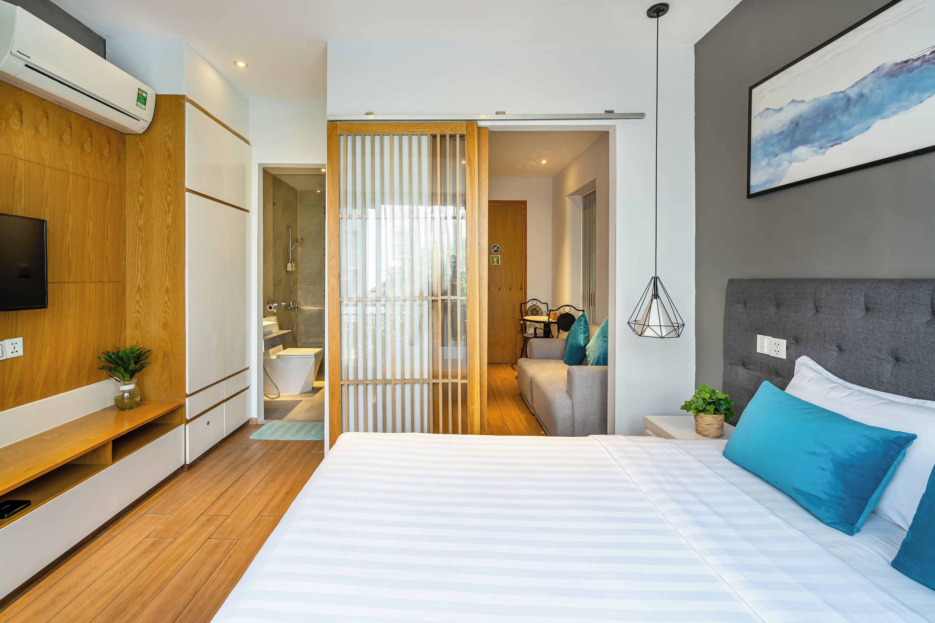 A modern bedroom with a large bed, a TV, a wooden wardrobe, and a bathroom visible through a sliding door.