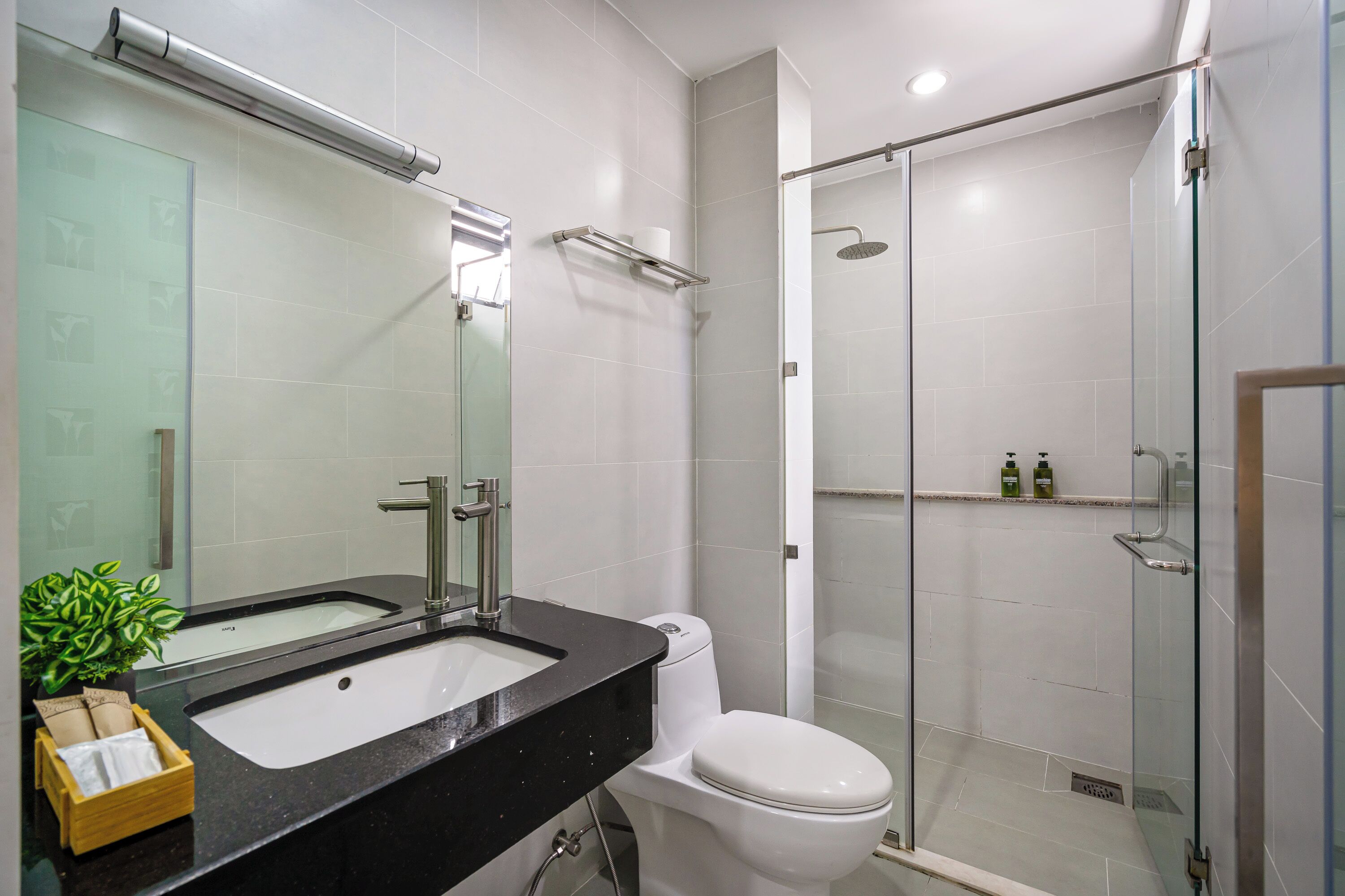 Une salle de bain moderne avec une douche à parois de verre, des toilettes blanches et un plan de toilette noir.