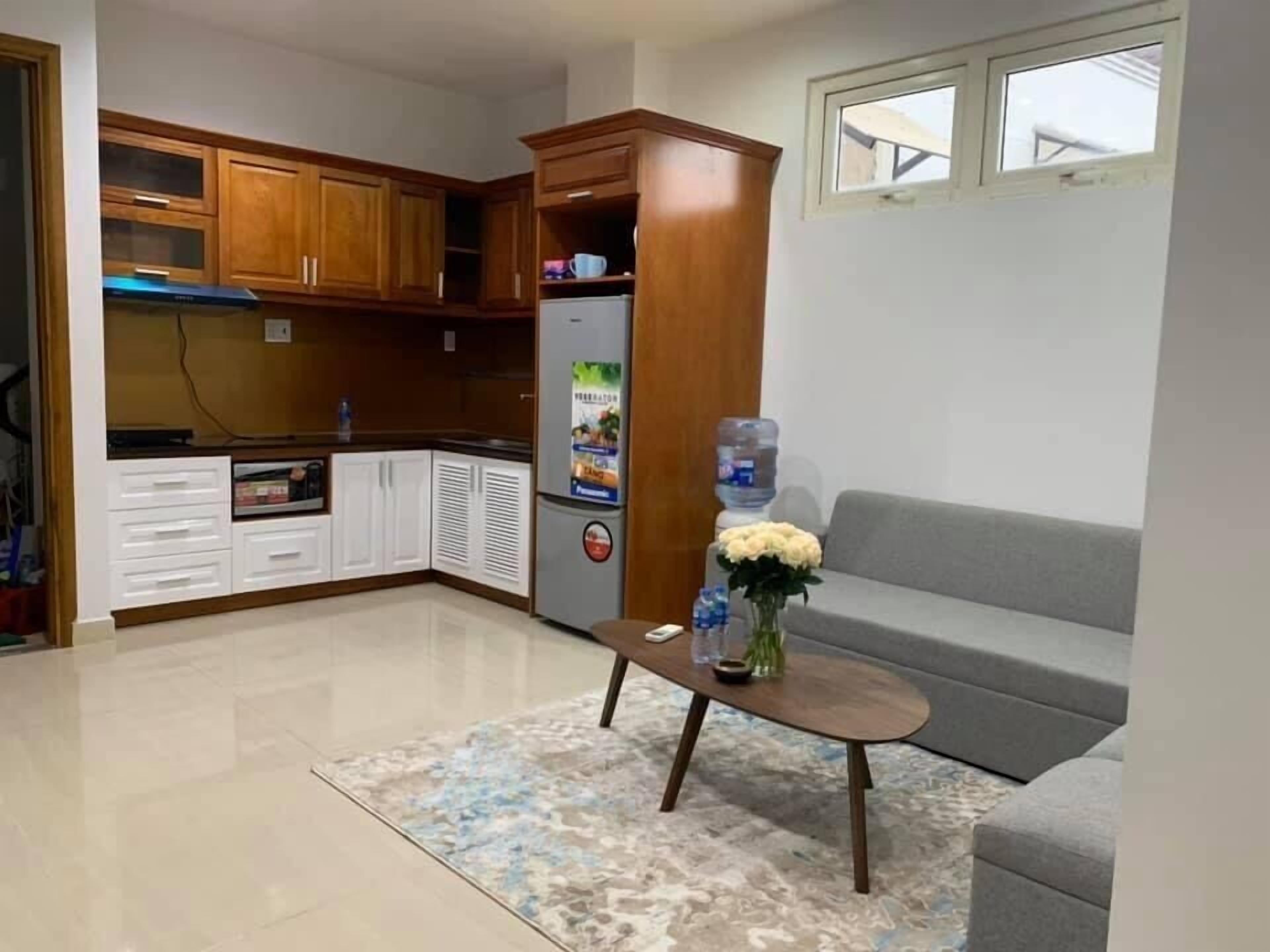 A compact living space with a kitchenette, a grey sofa, and a coffee table with a vase.
