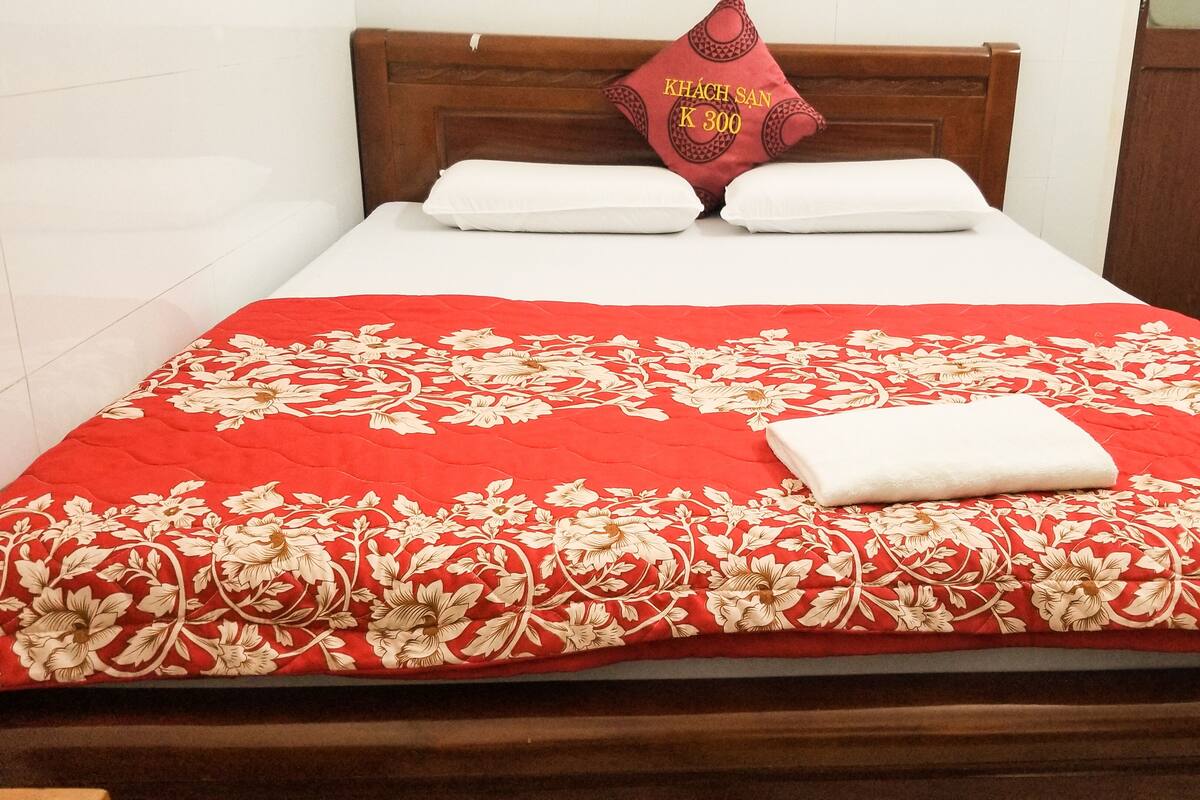 A bed with a red floral bedspread, two white pillows, and a red pillow with text.
