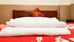 A bed with two white towels and a red pillow with text.