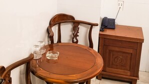 A corner room with a round wooden table, two chairs, a small wooden cabinet, and a wall-mounted television.