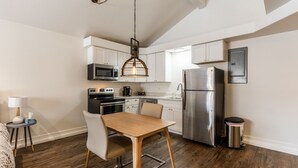 A modern kitchen with white cabinets, stainless steel appliances, a wooden dining table, and a hanging light fixture.