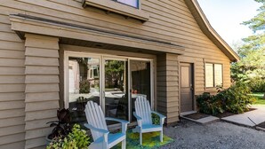 A house with a sliding glass door entrance, two Adirondack chairs outside, and a gravel driveway.