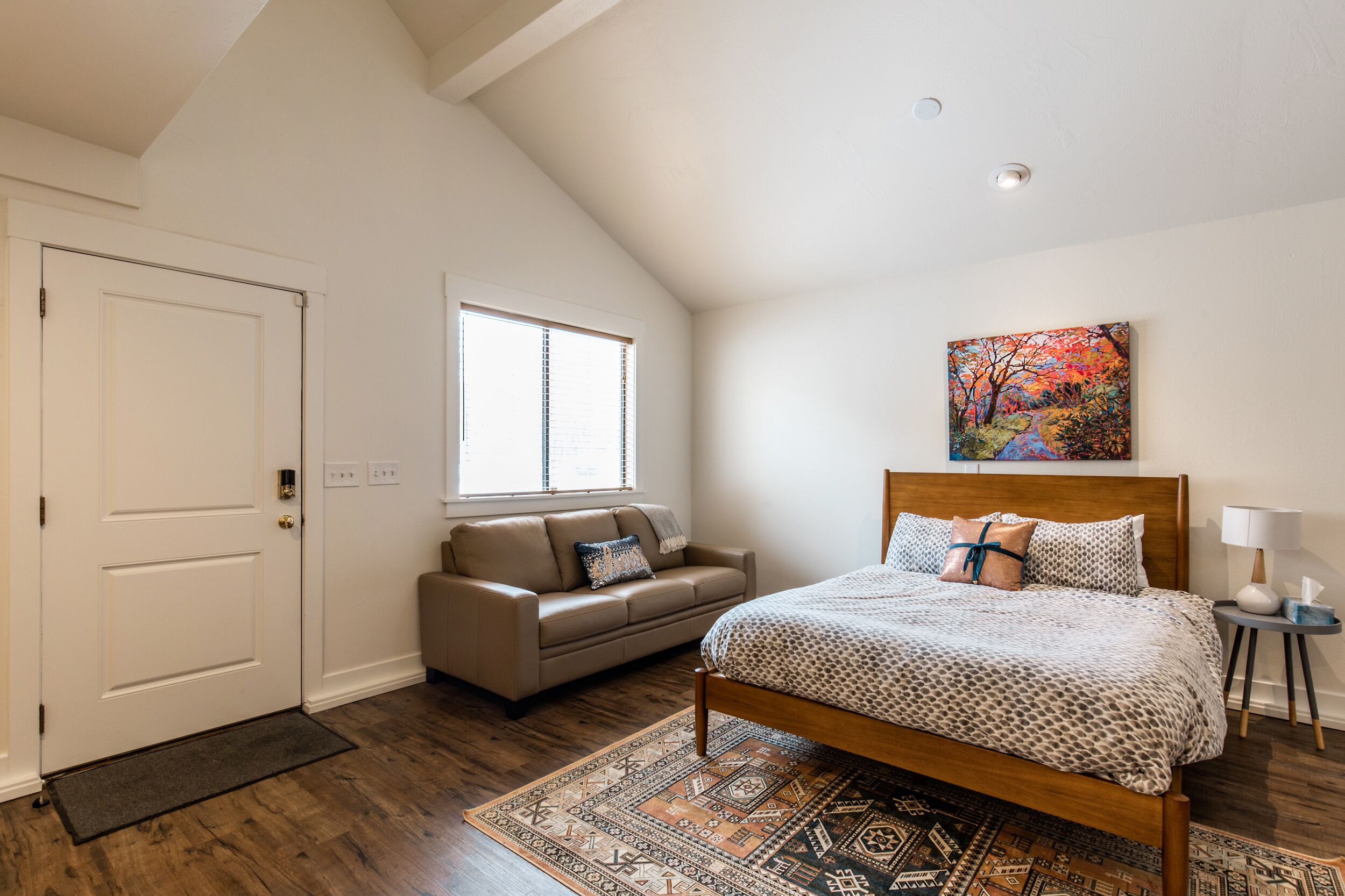 Quarto com cama, janela, quadro e uma mesa pequena com abajur.