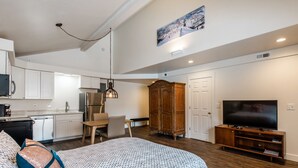 A modern apartment with a kitchenette, a dining area, a large bed, a TV, and a wardrobe.
