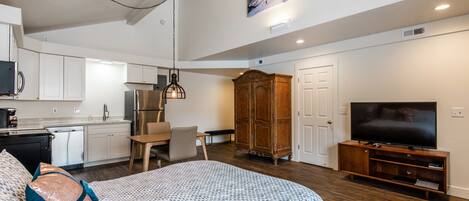 A modern apartment with a kitchenette, a dining area, a large bed, a TV, and a wardrobe.