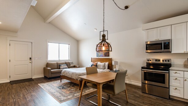 A spacious loft apartment with a dining area, a kitchen with modern appliances, a large window, and a high ceiling.