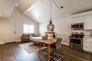 A spacious loft apartment with a dining area, a kitchen with modern appliances, a large window, and a high ceiling.