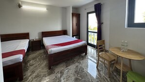 Een hotelkamer met twee bedden, een tafeltje, een stoel, een raam met gordijnen en een balkon.