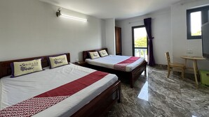 Een hotelkamer met twee bedden, een kleine tafel, een stoel, een plafondventilator en een raam met gordijnen.