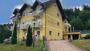 Un edificio giallo a più piani con balconi, un ingresso pavimentato e un cartello con la scritta "Velden Apartments".