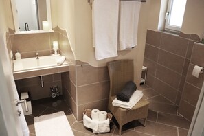 Een badkamer met een wastafel, spiegel, handdoekhouder, rieten stoel en een klein mandje met handdoeken.