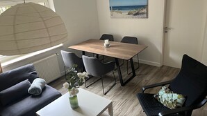 Un'area pranzo con un tavolo e sedie in legno, un vaso bianco con fiori, un divano grigio e una poltrona nera.