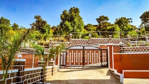 Una entrada protegida con muro de ladrillo y portón metálico, rodeada de árboles y cielo despejado.