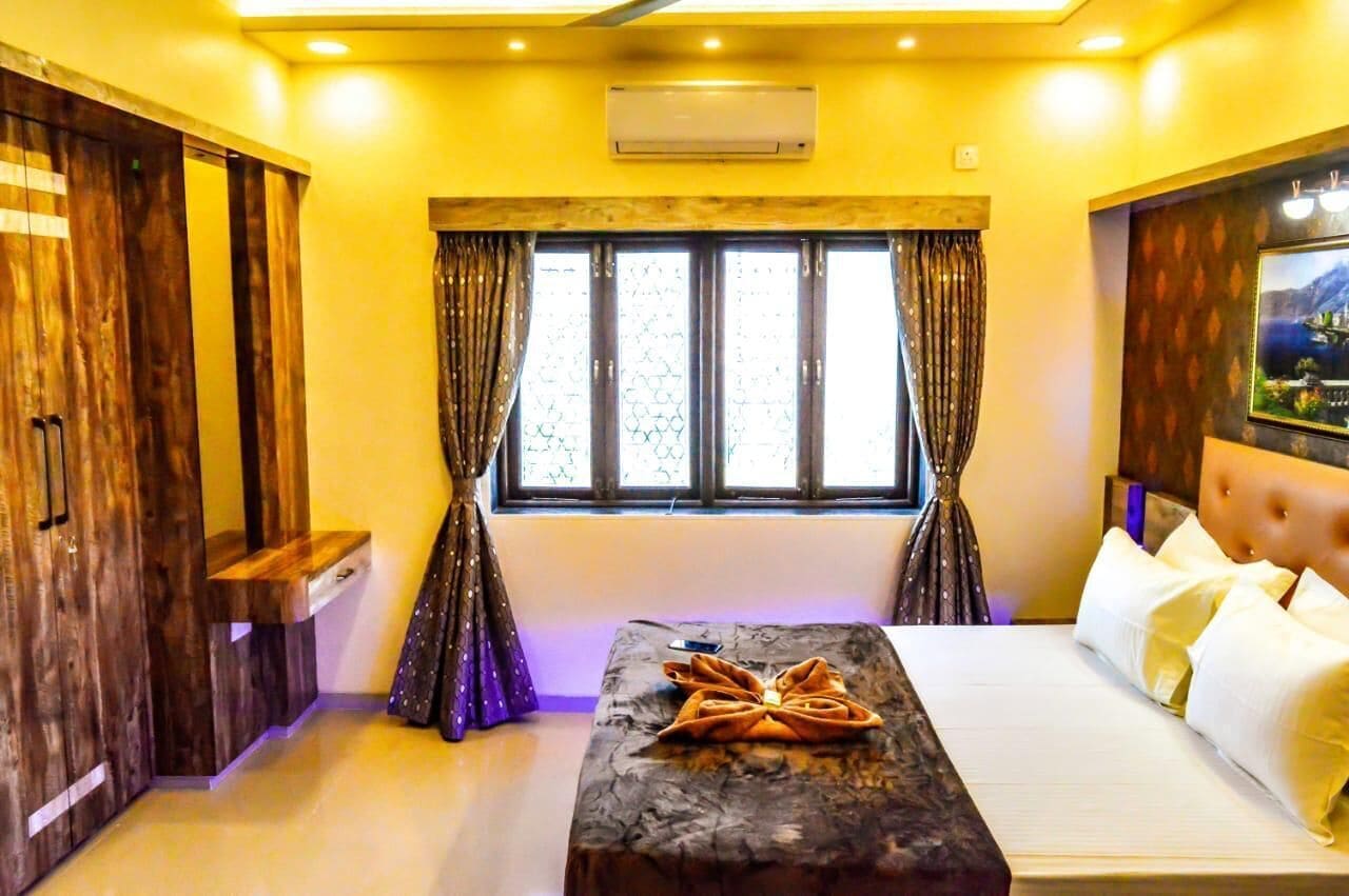 Une chambre d’hôtel avec un lit, une table de chevet, une fenêtre avec des rideaux et un téléviseur fixé au mur.
