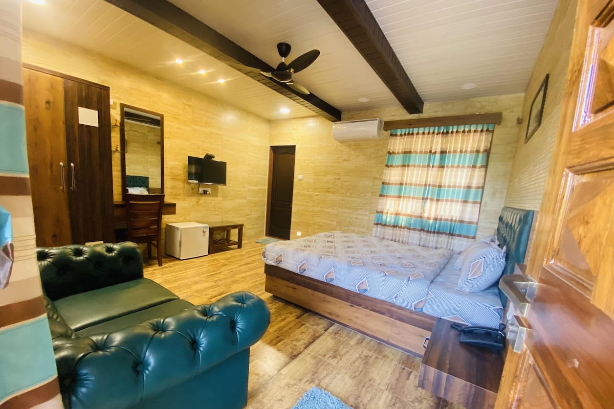 A bedroom with a bed, a sofa, a TV, a ceiling fan, and a small table.
