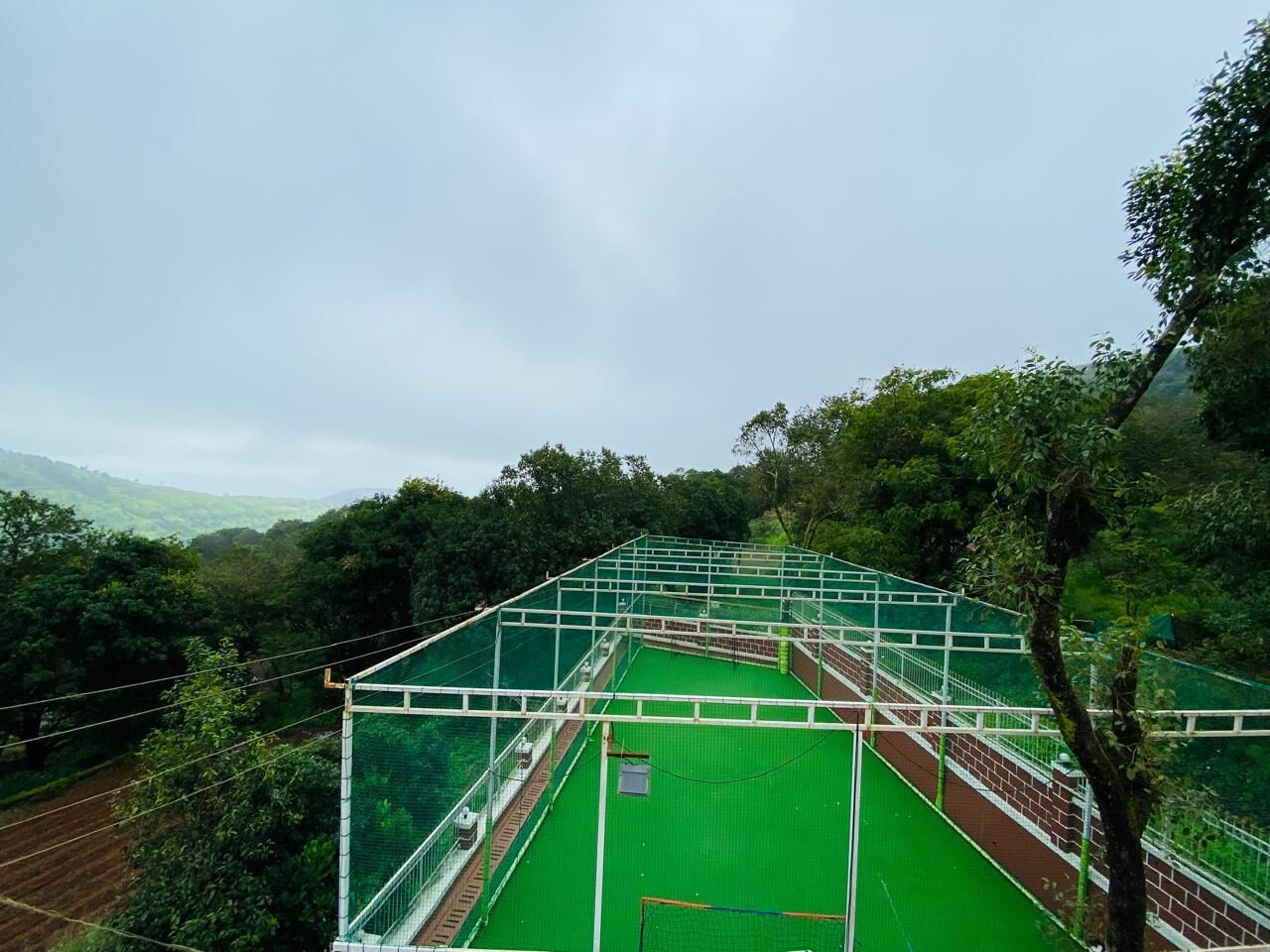 A tennis court with a green surface, surrounded by trees and a cloudy sky.