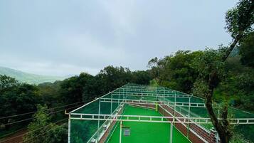 A tennis court with a green surface, surrounded by trees and a cloudy sky.