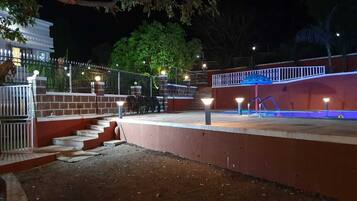 Een buitengebied bij nacht, met trappen die leiden naar een platform, omringd door een hek en verlicht door straatlantaarns.
