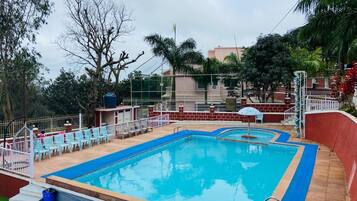 A swimming pool with blue and white tiles, surrounded by a white fence and a few chairs.