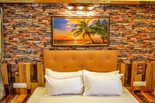 Une chambre avec un mur en pierre, un tableau représentant un coucher de soleil et un palmier, et une tête de lit capitonnée.