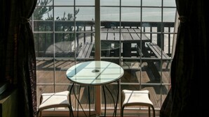 A room with a large window overlooking a wooden deck and the sea. There is a round glass table with two chairs in front. - Badasol Fragrance Pension (Taean)